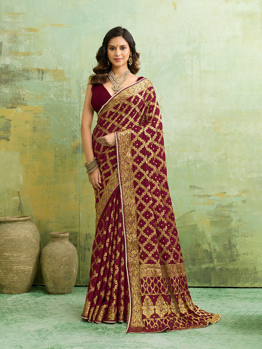 A maroon and gold Banarasi silk saree with heavy zari work (embroidery) and mirror handwork. The saree is traditional wear, likely used for festive or bridal occasions.