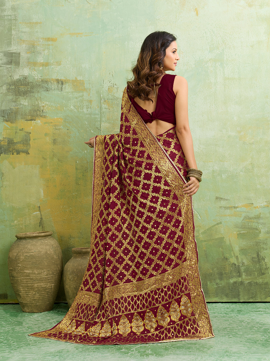 A maroon and gold Banarasi silk saree with heavy zari work (embroidery) and mirror handwork. The saree is traditional wear, likely used for festive or bridal occasions.