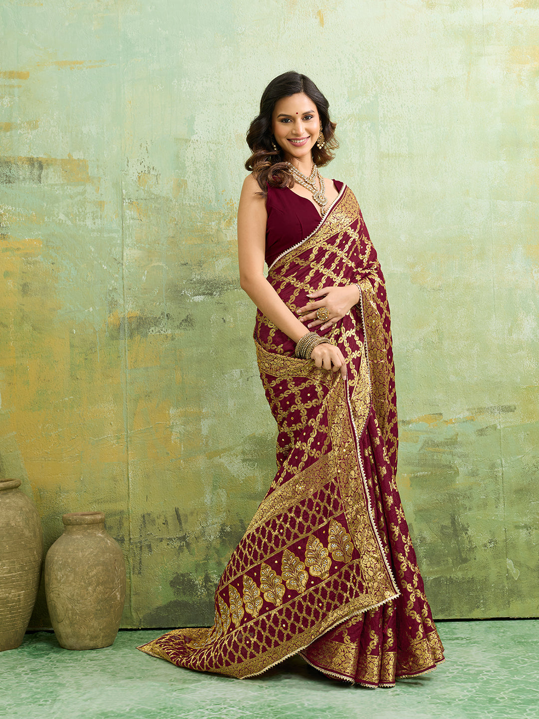 A maroon and gold Banarasi silk saree with heavy zari work (embroidery) and mirror handwork. The saree is traditional wear, likely used for festive or bridal occasions.