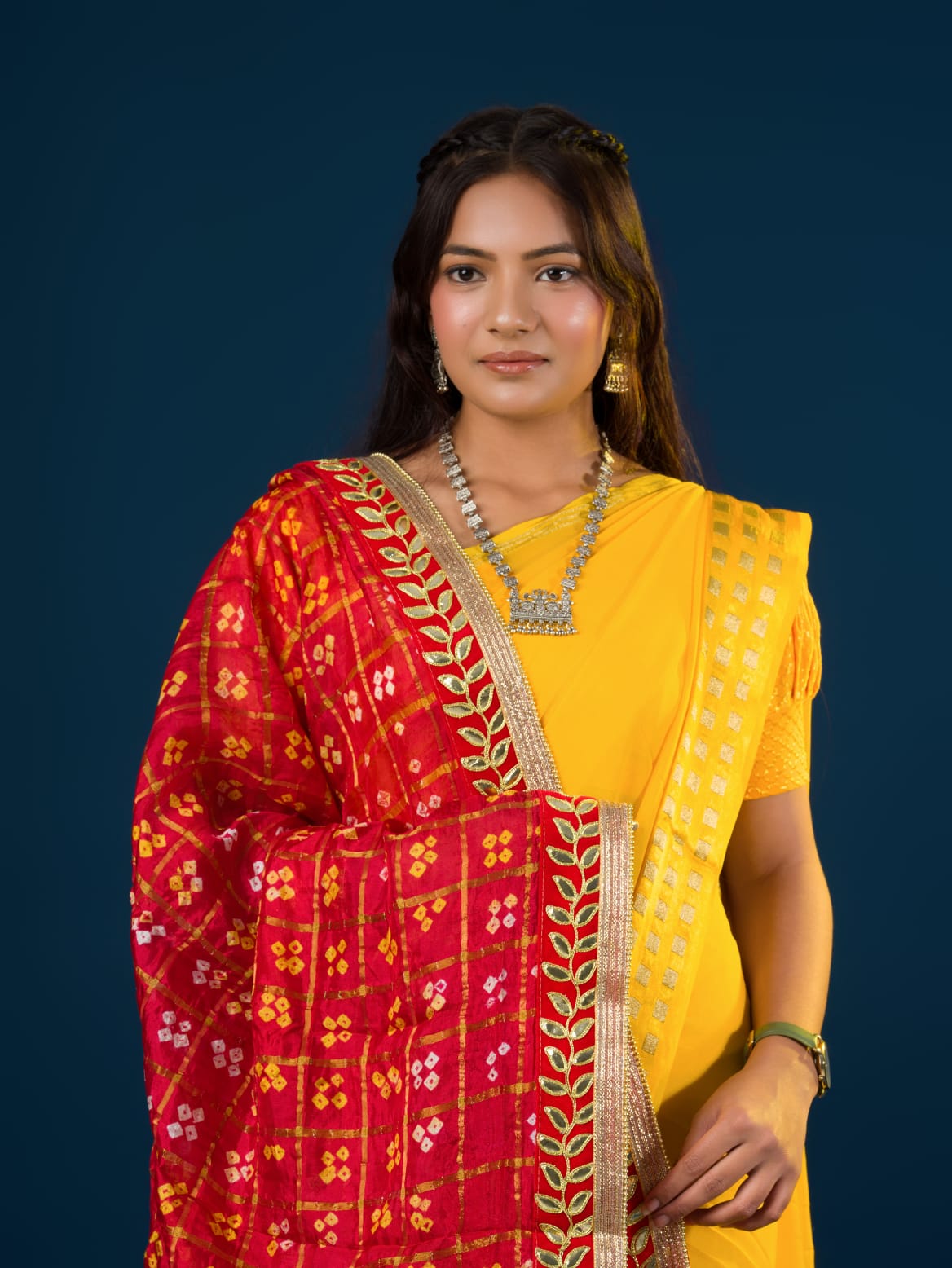 A woman in a traditional yellow attire is holding a red and yellow Bandhani silk chunri with floral patterns and a border.