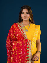 A woman in a traditional yellow attire is holding a red and yellow Bandhani silk chunri with floral patterns and a border.