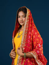 A woman in a traditional yellow attire is holding a red and yellow Bandhani silk chunri with floral patterns and a border.
