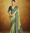 A green and peach banarasi silk saree with floral and geometric patterns and hand embellishments.