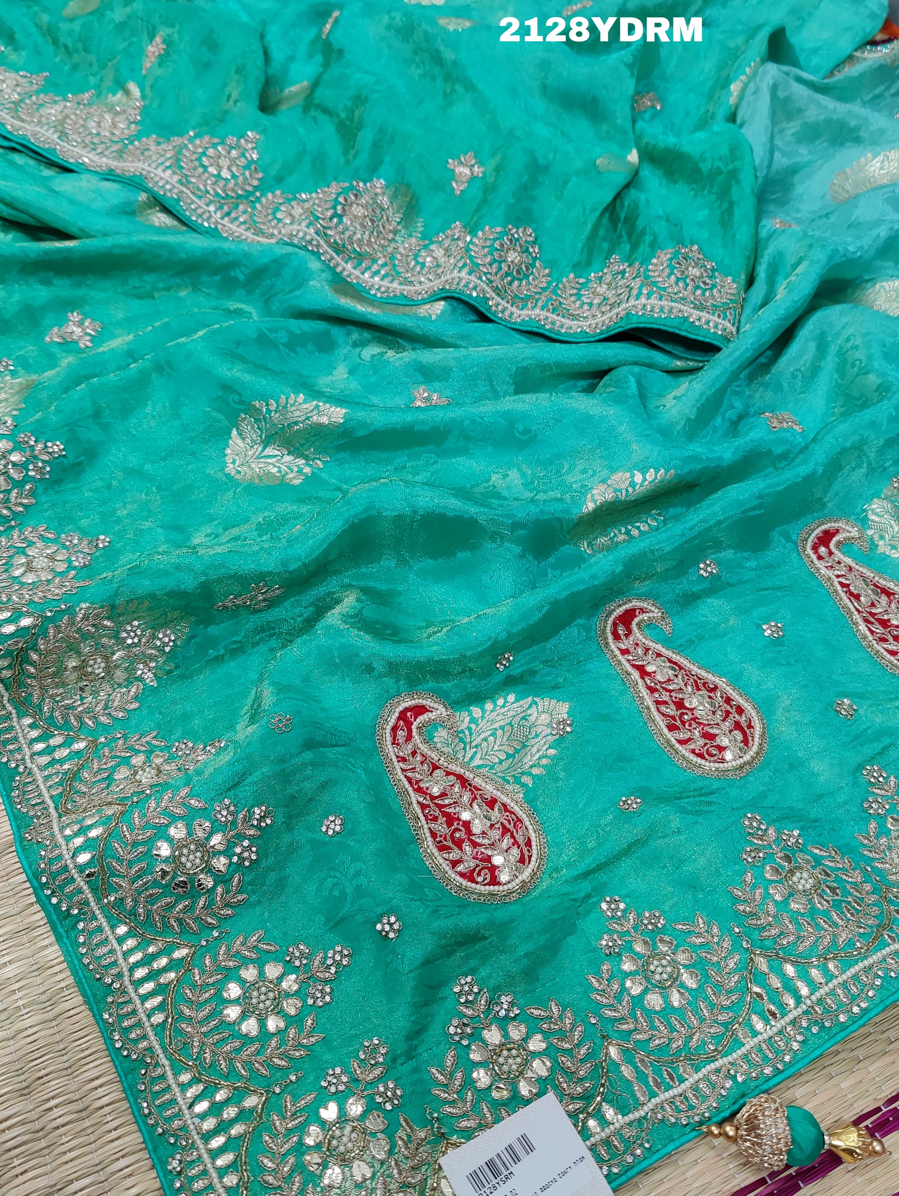A green saree with red and silver paisley patterns and detailed embroidery,