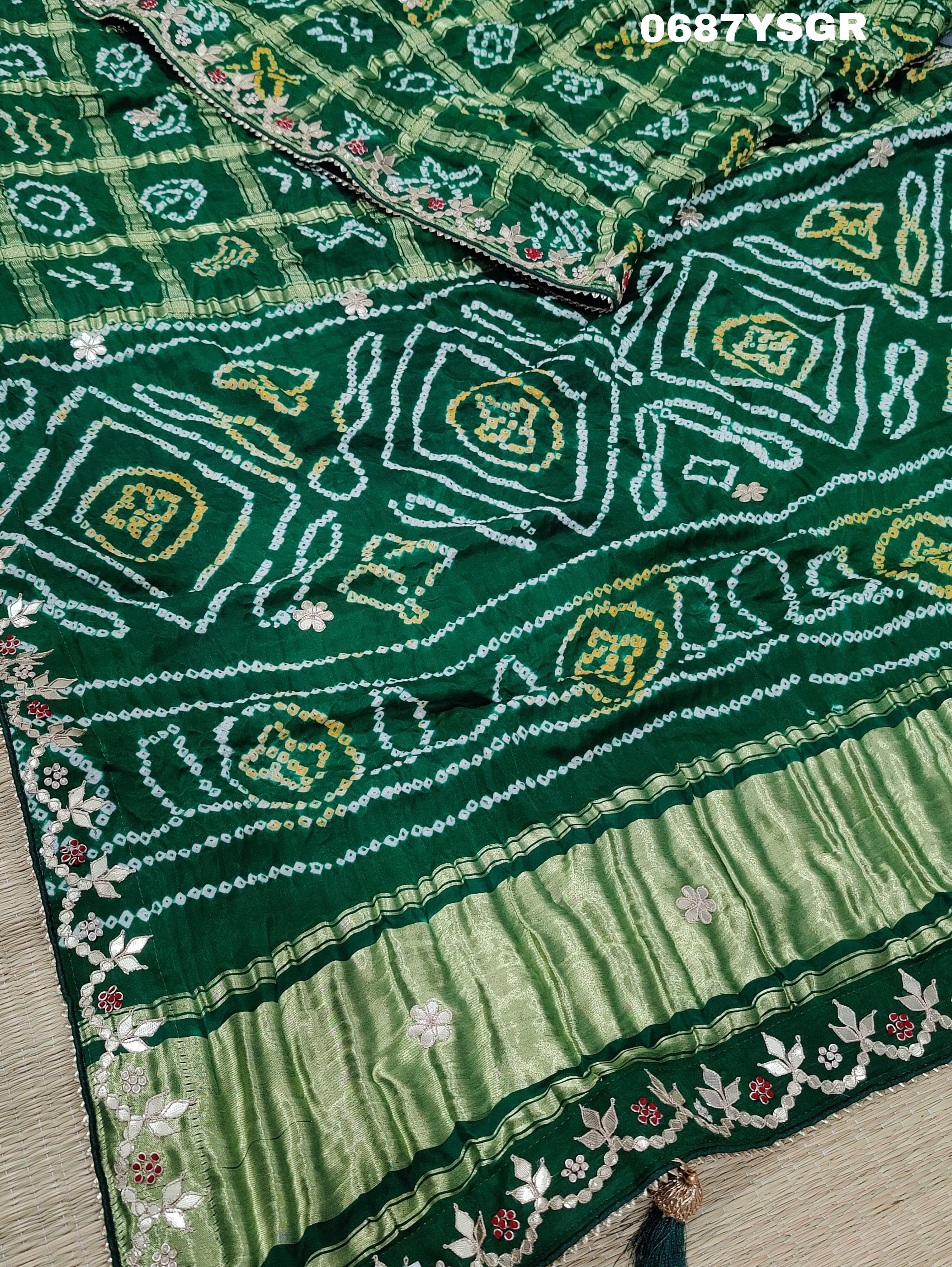A green and silver pure gaji silk saree with bandhani pattern and gotapatti handwork, displayed on a surface.