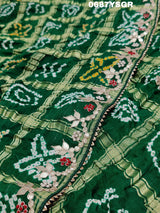 A green and silver pure gaji silk saree with bandhani pattern and gotapatti handwork, displayed on a surface.