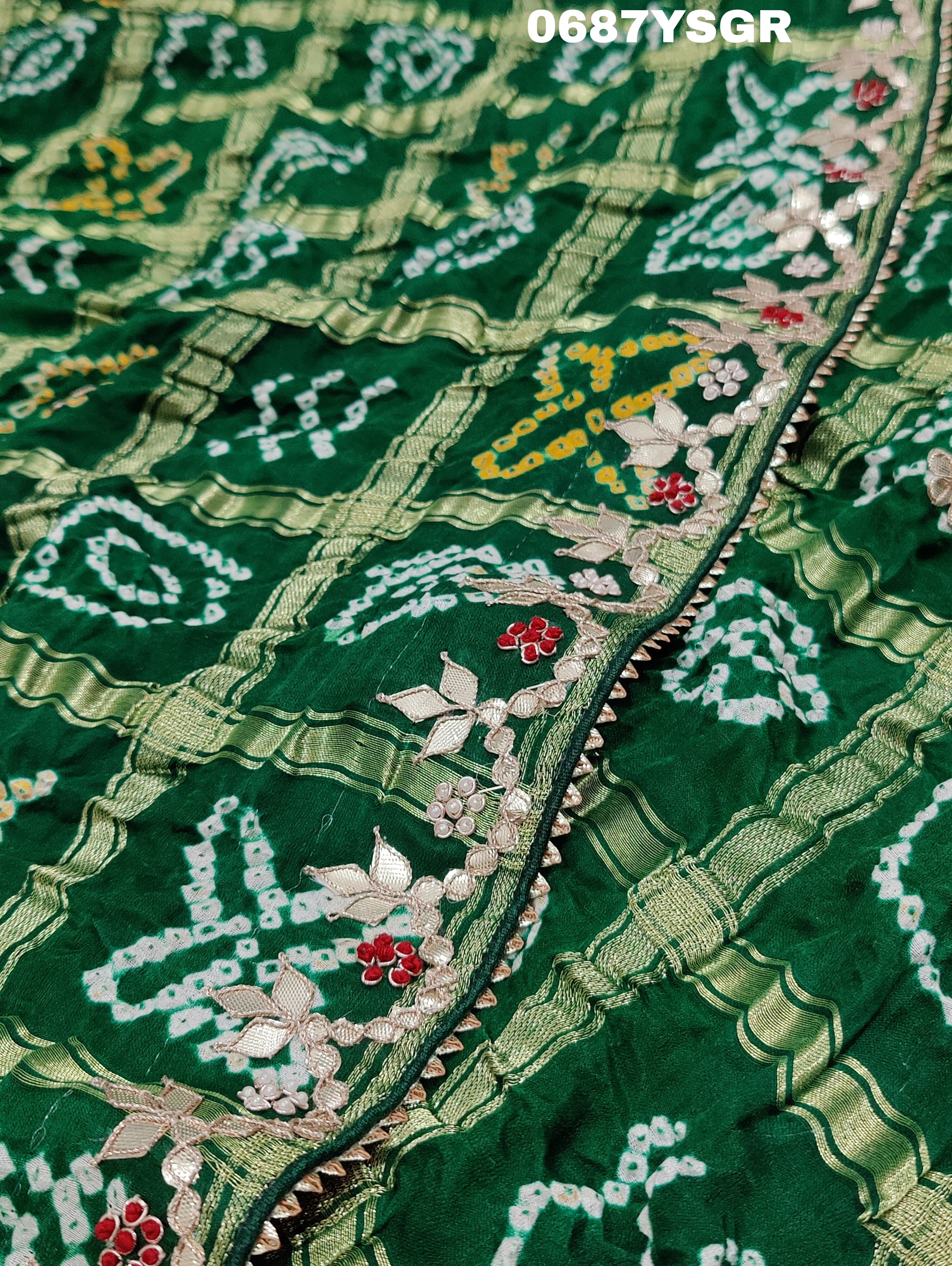 A green and silver pure gaji silk saree with bandhani pattern and gotapatti handwork, displayed on a surface.