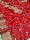 A red and silver bandhani style silk saree with mirror handwork, including floral patterns and a traditional design.