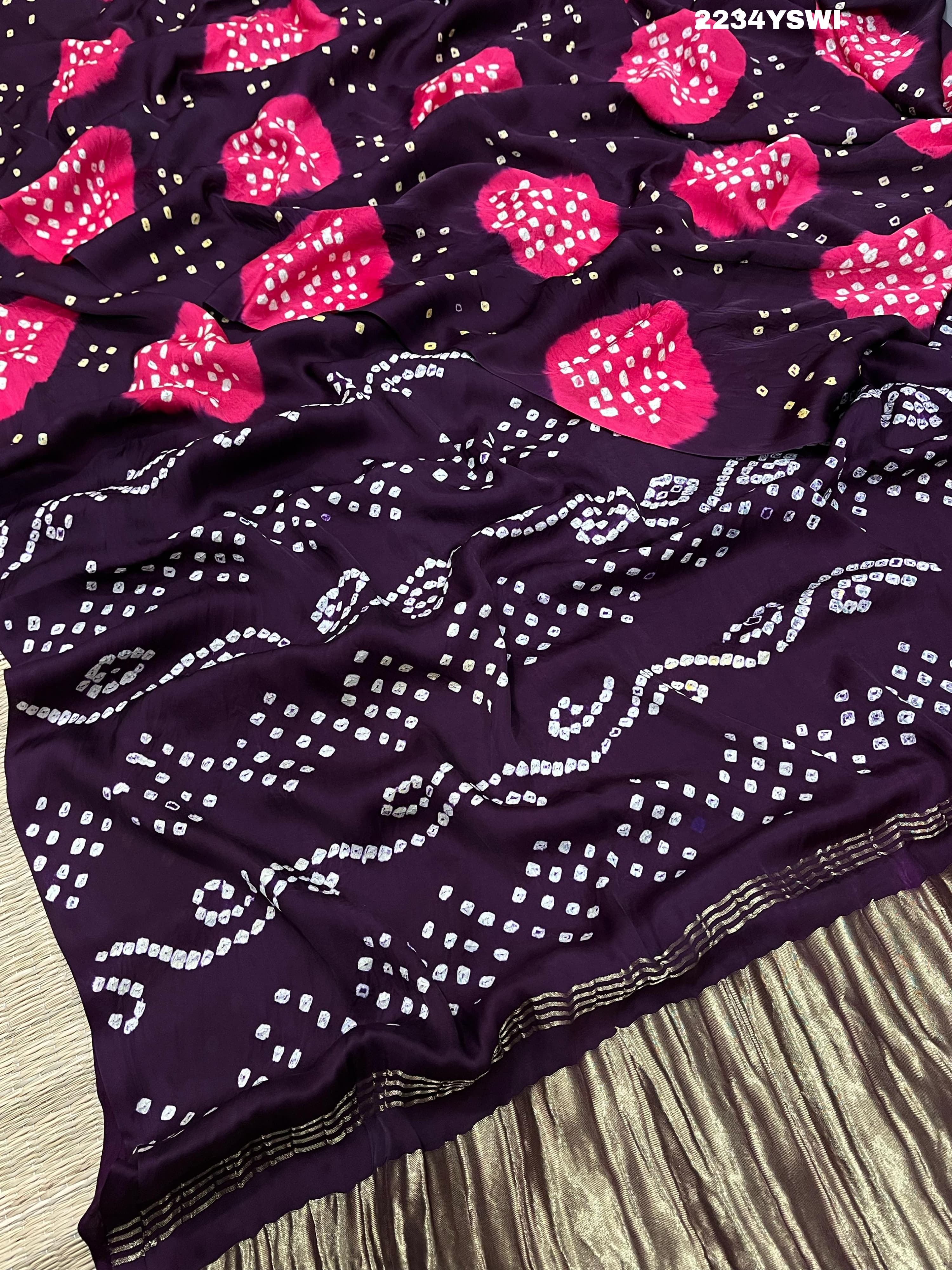 A purple and pink bandhani style saree with detailed patterns and a golden border.