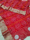 A red and silver bandhani style Dola silk saree with cutdana work and floral patterns, along with a golden border.