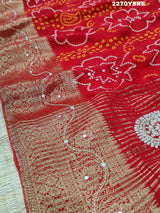 A red and silver bandhani style Dola silk saree with cutdana work and floral patterns, along with a golden border.
