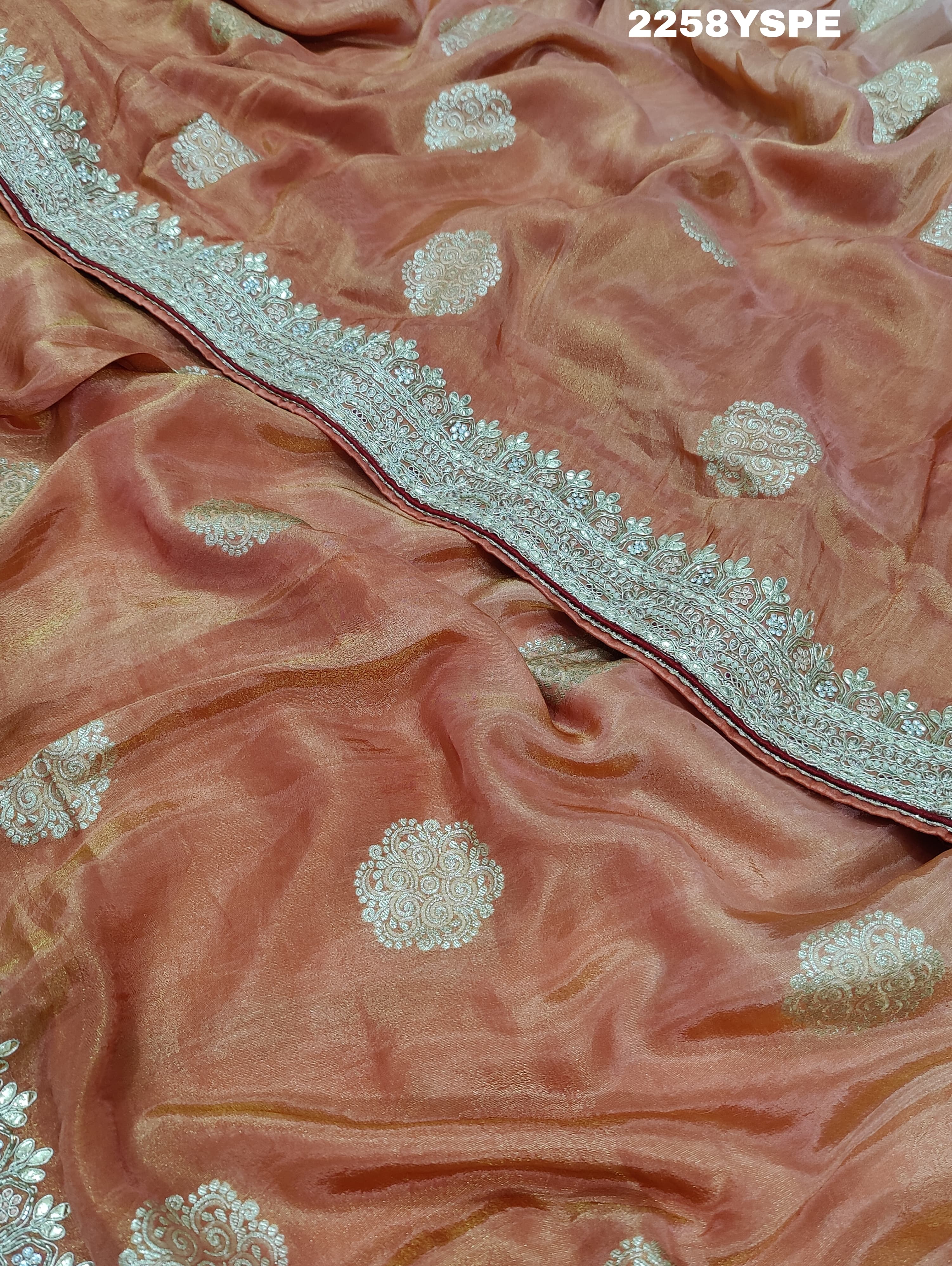 A peach-colored Banarasi silk saree with Bollywood-style embellishments including sequins and gotapatti work,