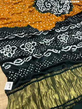 A bandhani style saree with black and yellow patterns on a fabric surface.