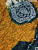 A bandhani style saree with black and yellow patterns on a fabric surface.