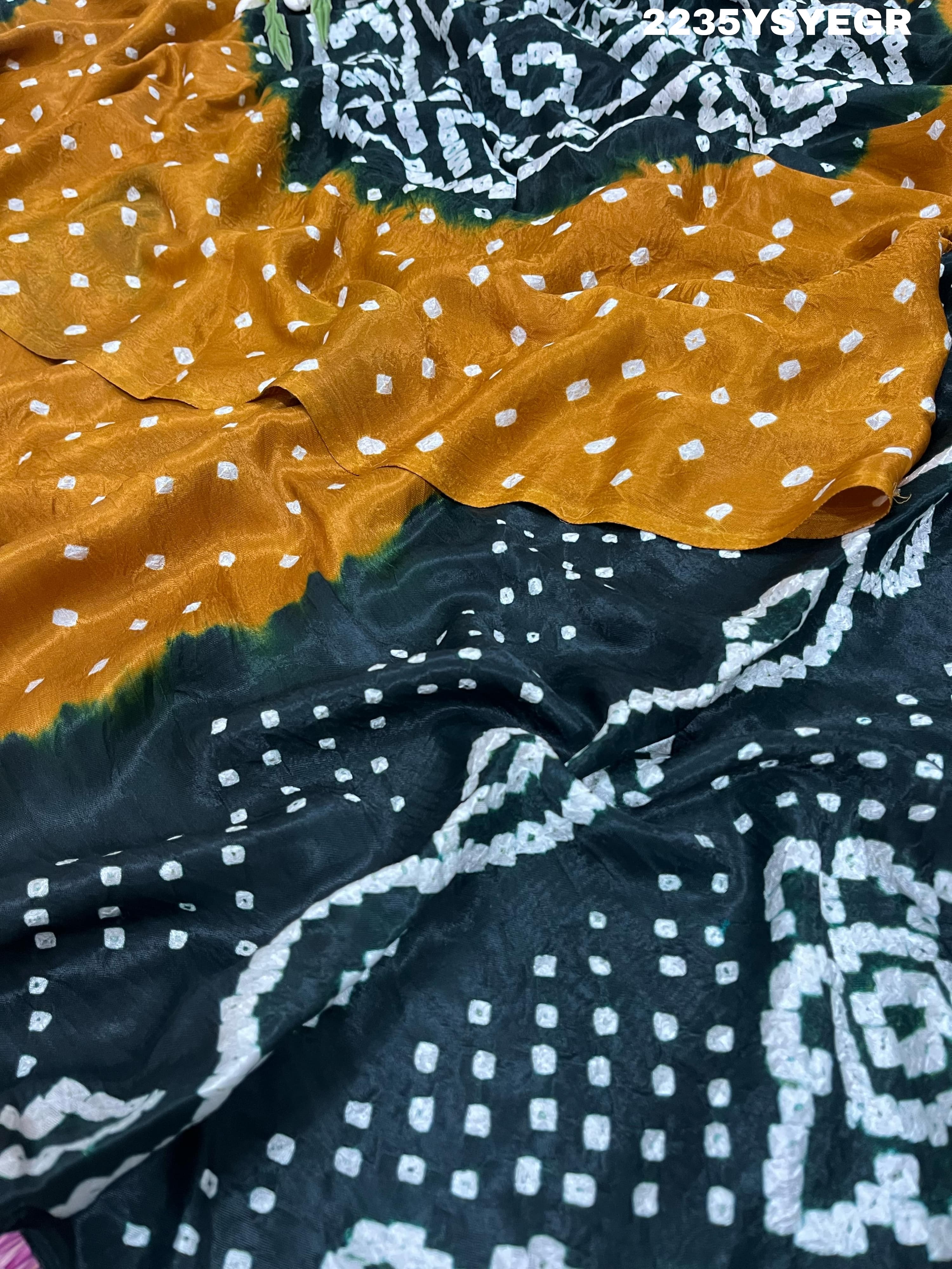 A bandhani style saree with black and yellow patterns on a fabric surface.