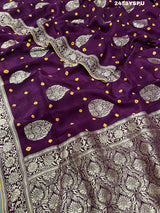 A purple Dola silk saree with detailed Zari weaving work and a Banarasi style pattern, including a wide border with similar ornate design.