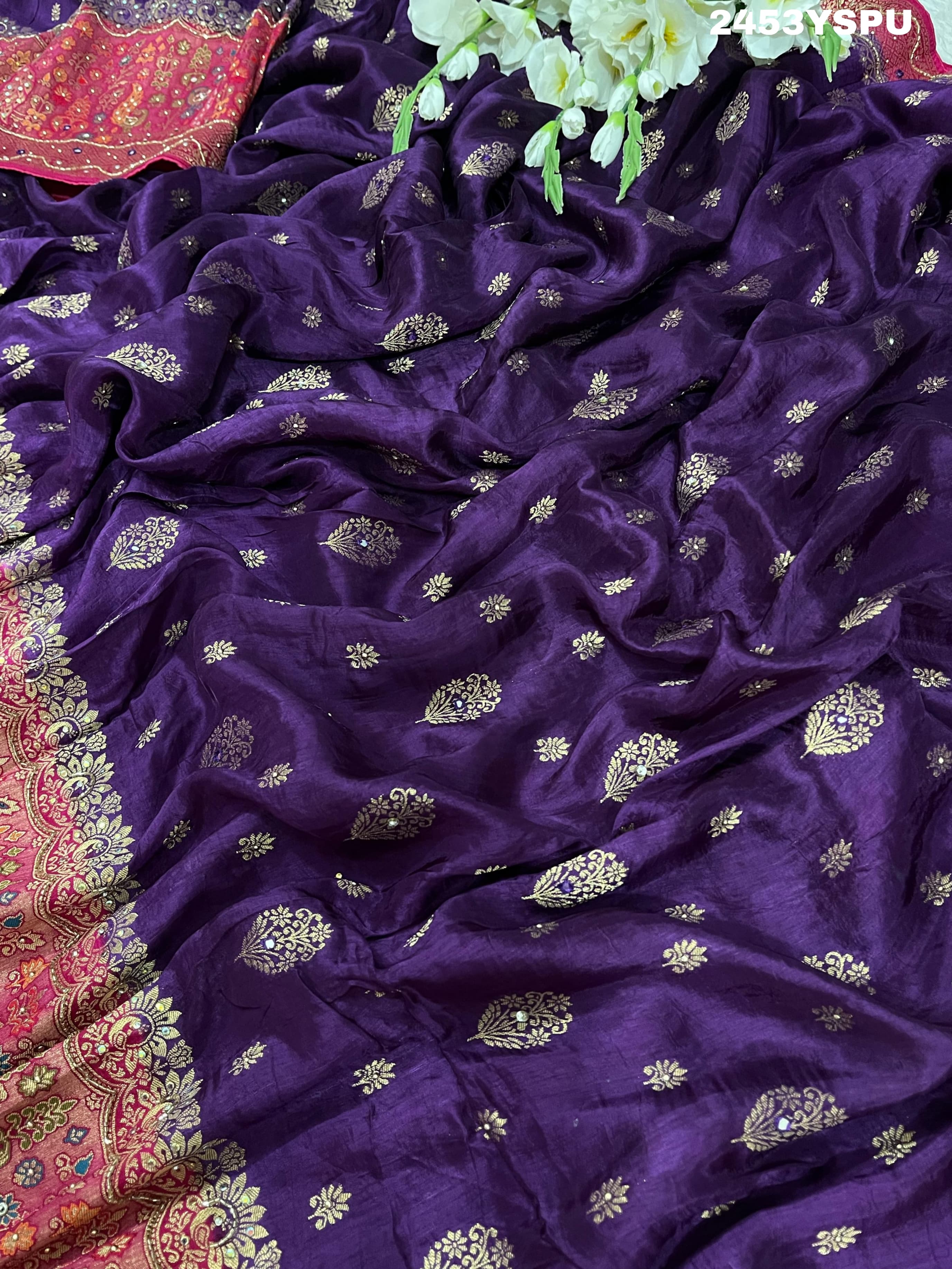 A purple and red Dola silk Banarasi saree with cutdana work, captured with a floral design at the border.