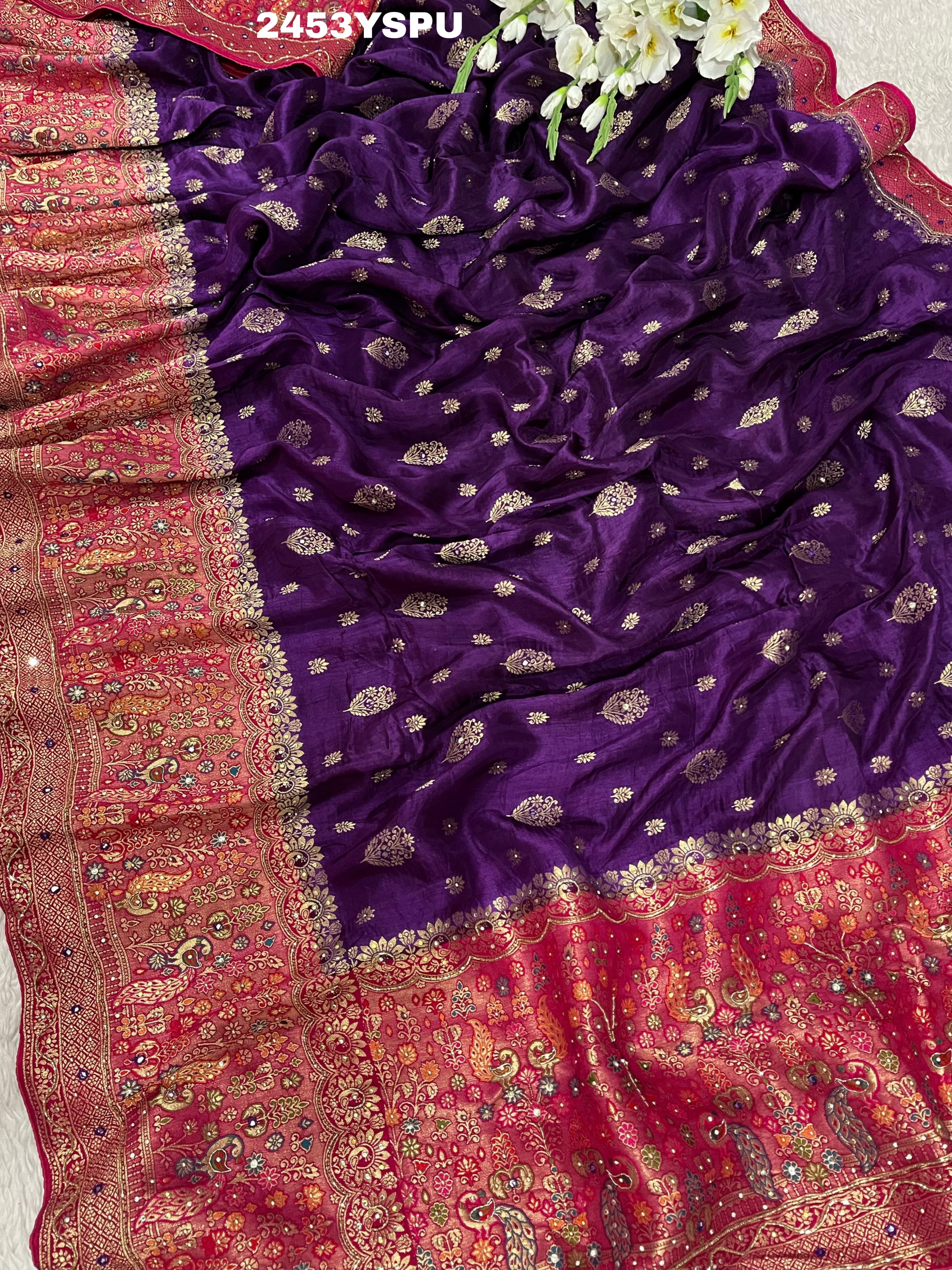 A purple and red Dola silk Banarasi saree with cutdana work, captured with a floral design at the border.