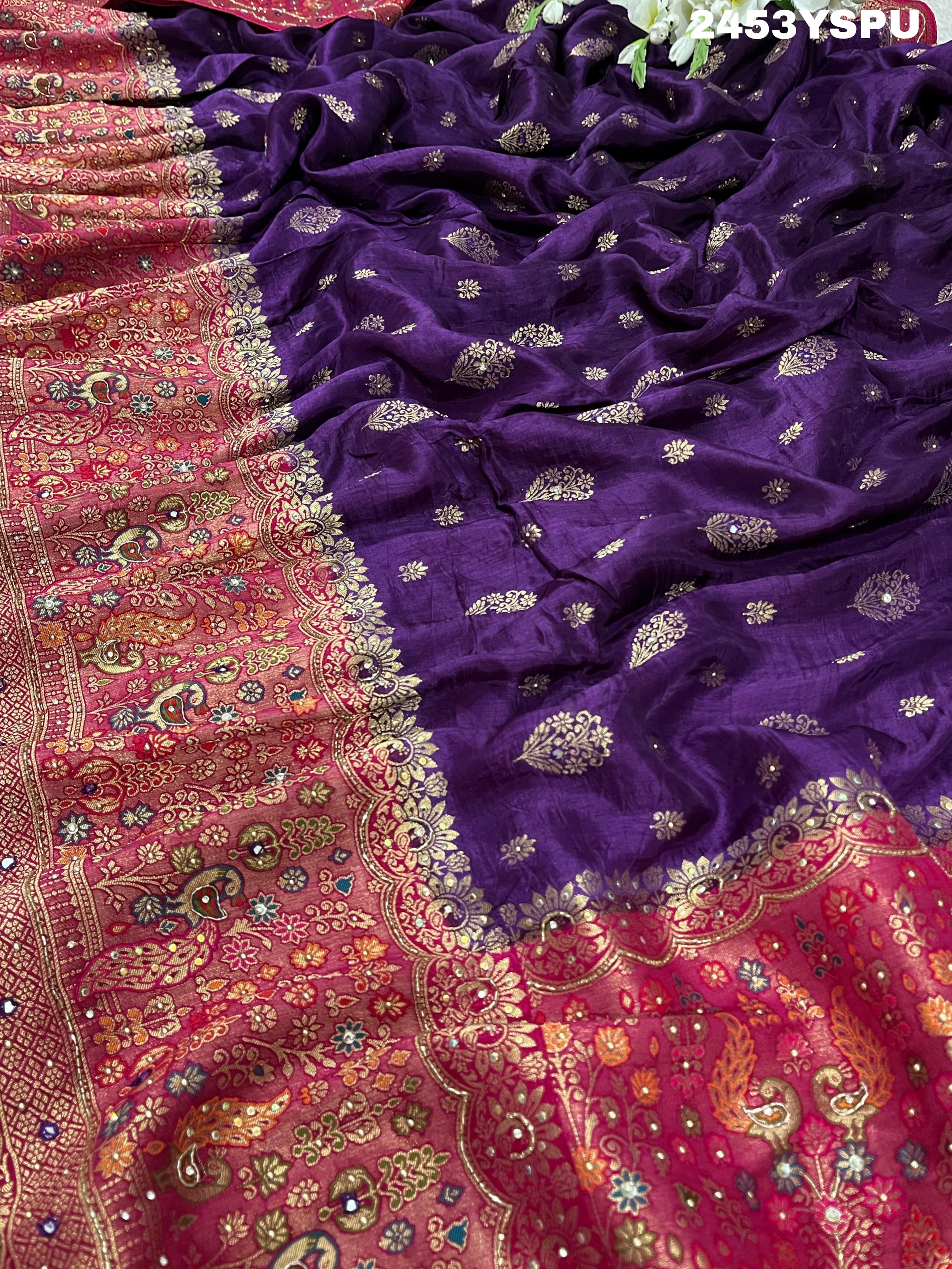 A purple and red Dola silk Banarasi saree with cutdana work, captured with a floral design at the border.