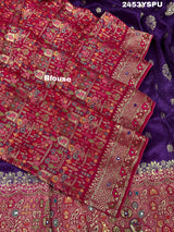 A purple and red Dola silk Banarasi saree with cutdana work, captured with a floral design at the border.