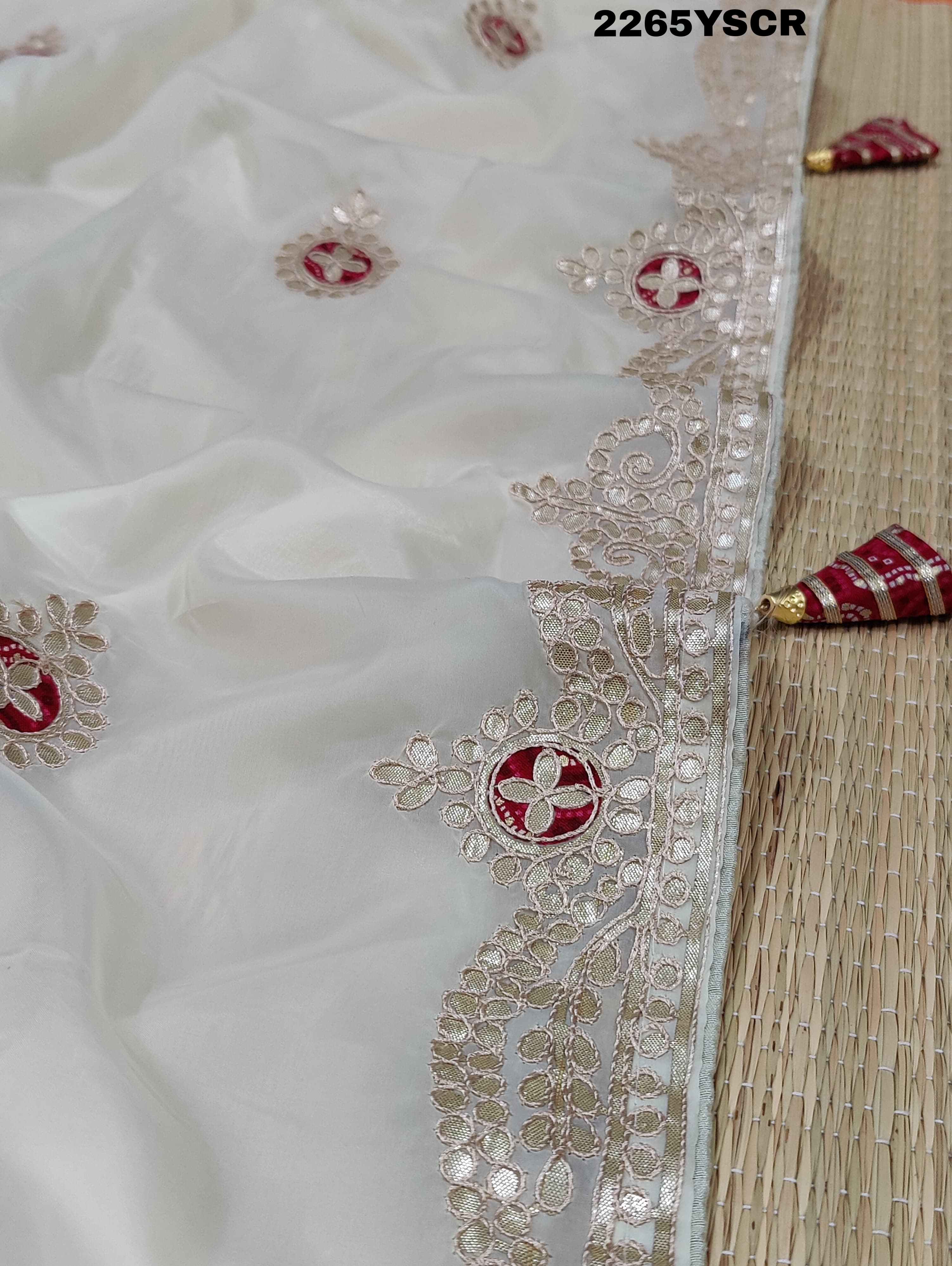 A cream-colored tissue silk saree with Bollywood-style embellishments and gotapatti work, including floral patterns and traditional border designs.