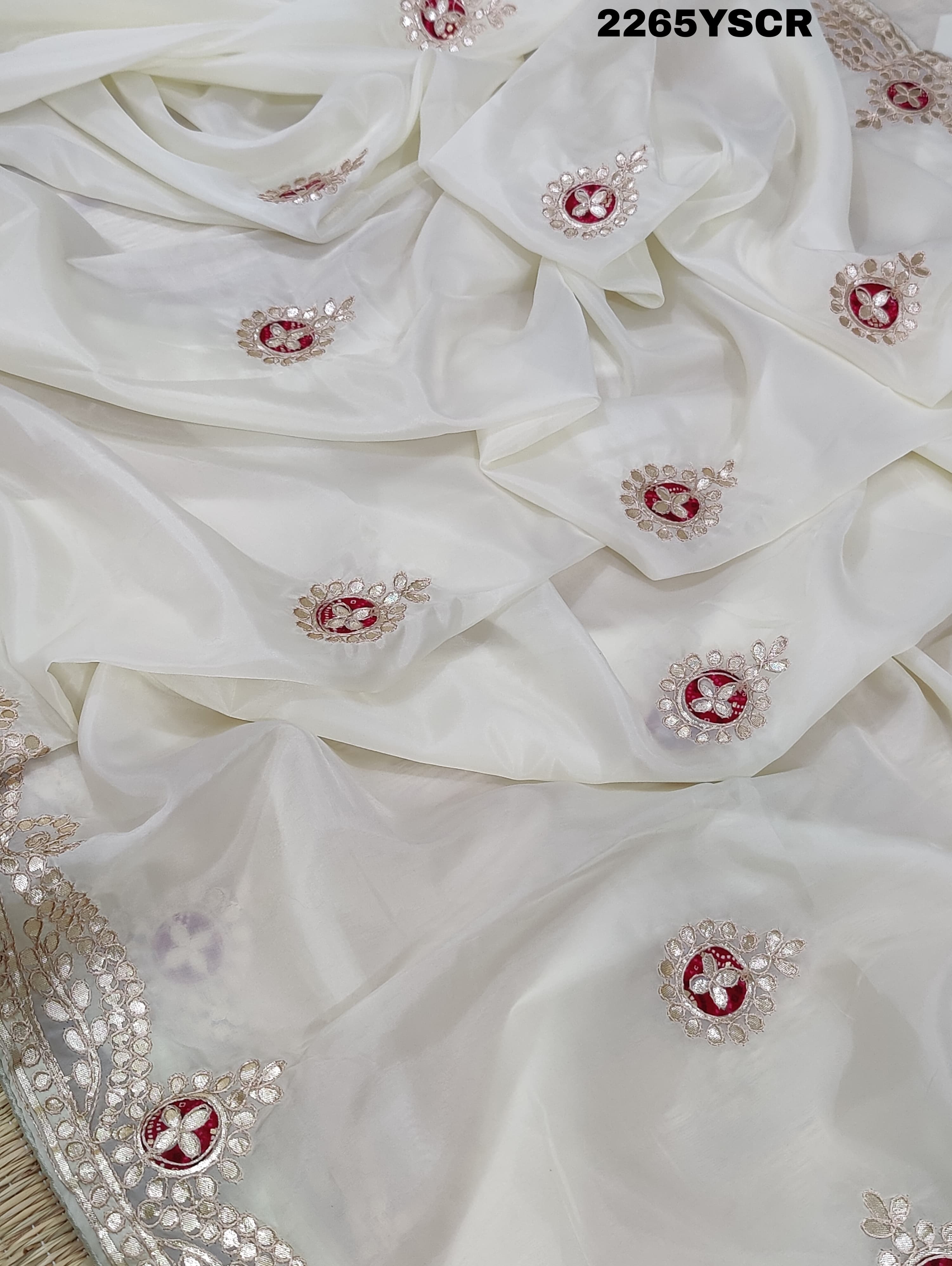 A cream-colored tissue silk saree with Bollywood-style embellishments and gotapatti work, including floral patterns and traditional border designs.