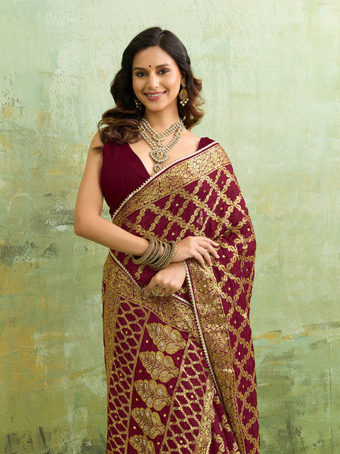  A maroon and gold Banarasi silk saree with heavy zari work (embroidery) and mirror handwork. The saree is traditional wear, likely used for festive or bridal occasions.