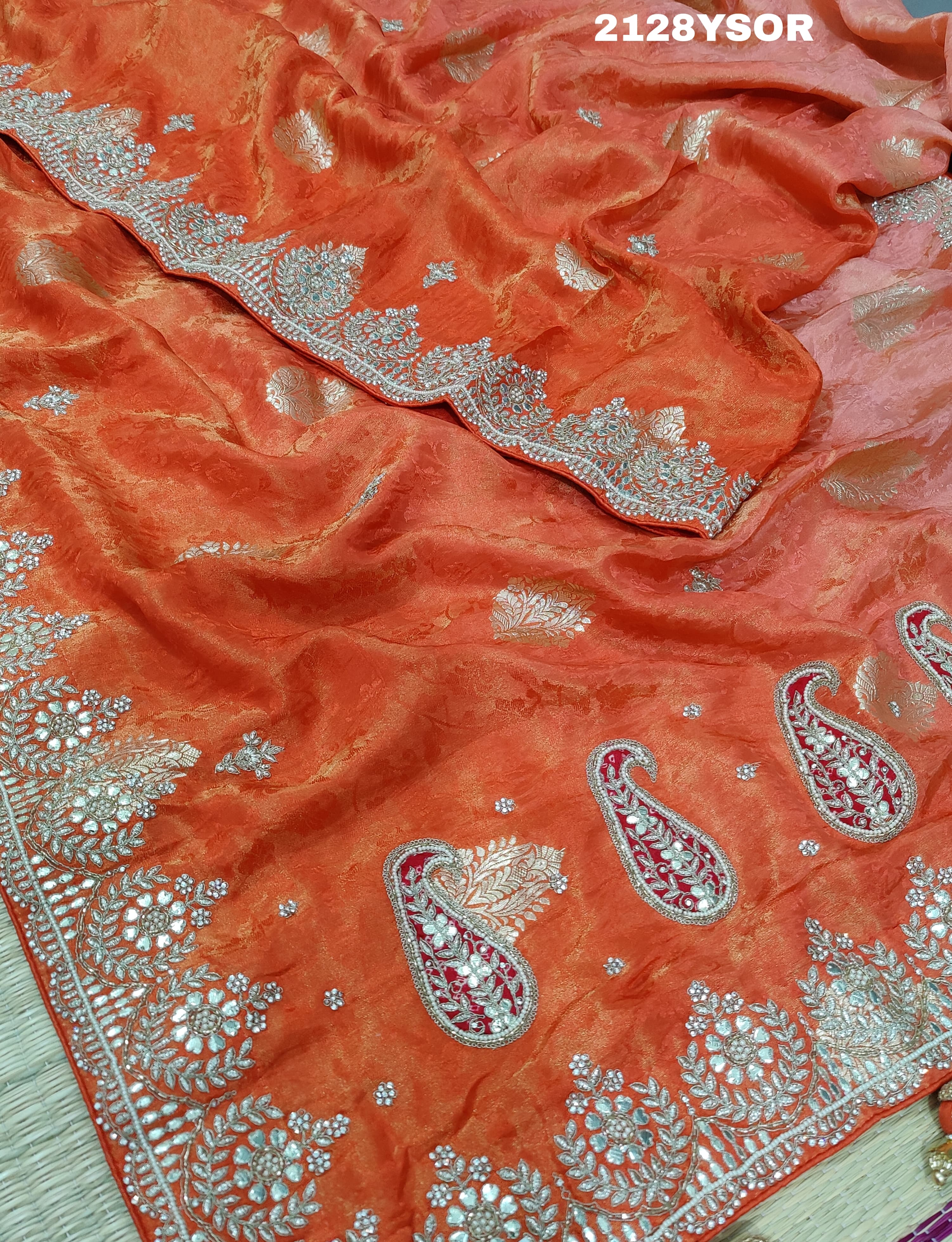 An orange saree with silver paisley pattern and floral gotapatti work, along with sequence embellishments.