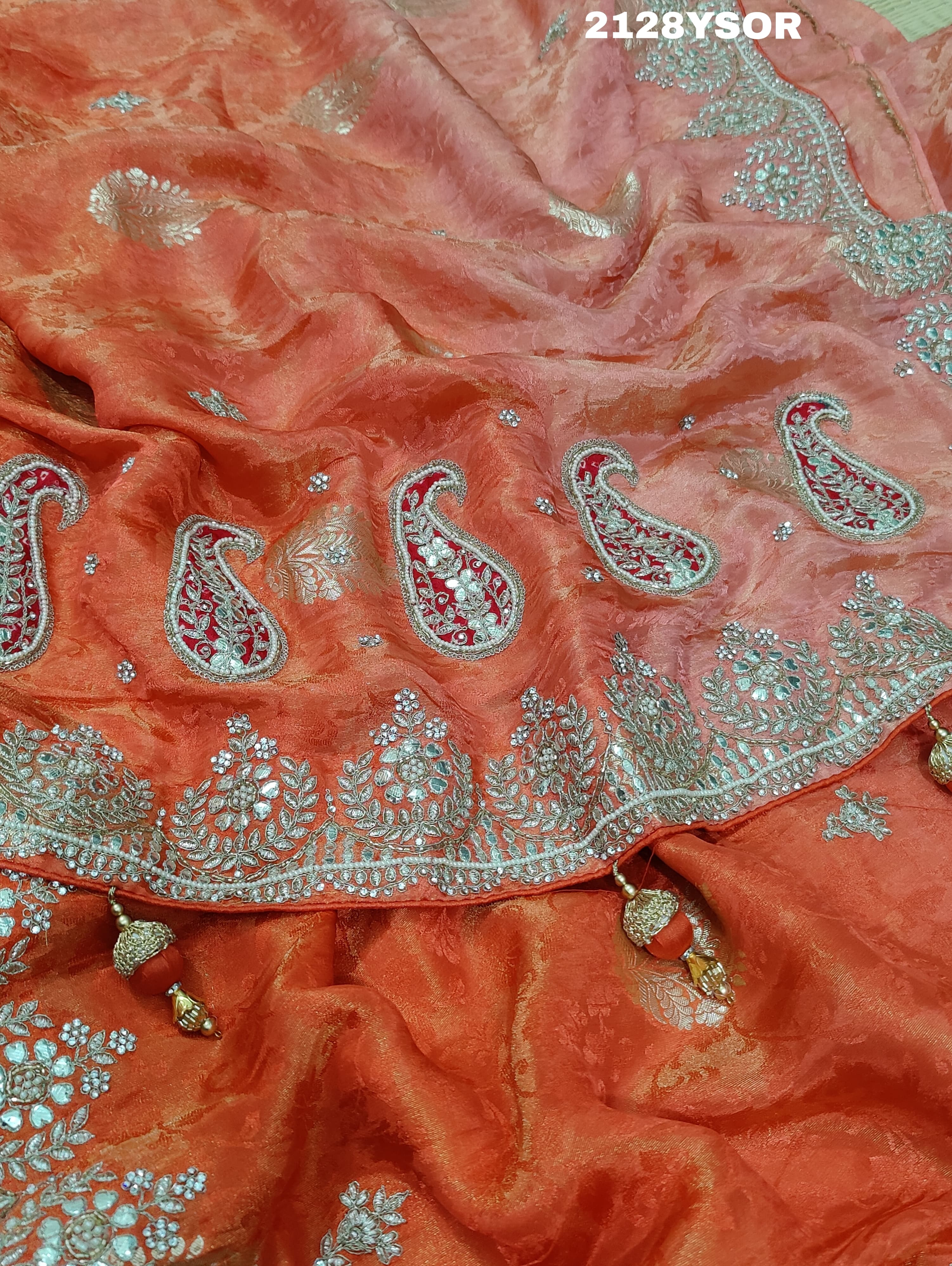 An orange saree with silver paisley pattern and floral gotapatti work, along with sequence embellishments.