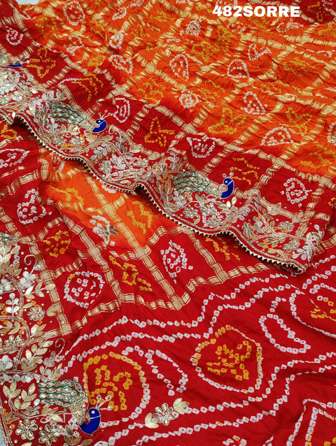 A red and orange pure gaji silk saree with bandhani style embellishments and heavy gotapatti work, along with a golden border and blue details.