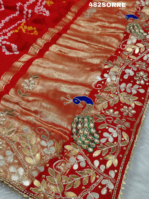 A red and orange pure gaji silk saree with bandhani style embellishments and heavy gotapatti work, along with a golden border and blue details.