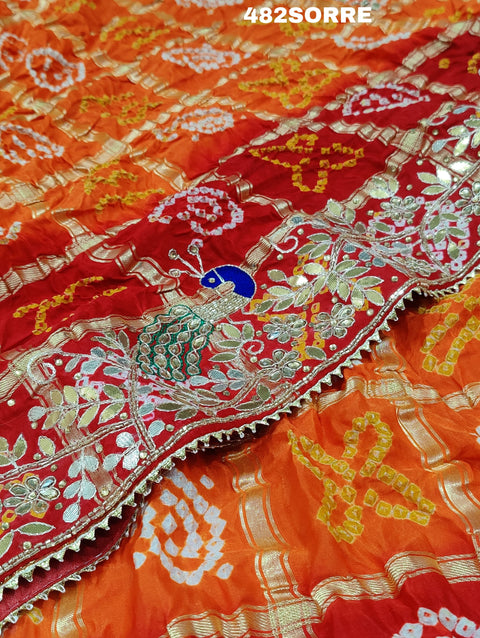 A red and orange pure gaji silk saree with bandhani style embellishments and heavy gotapatti work, along with a golden border and blue details.