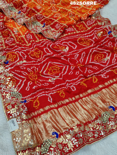A red and orange pure gaji silk saree with bandhani style embellishments and heavy gotapatti work, along with a golden border and blue details.
