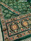 A green bandhej saree with royal aari and real mirror work, displayed on a surface.