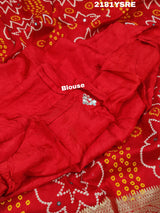 A red and silver bandhani style silk saree with mirror handwork, including floral patterns and a traditional design.