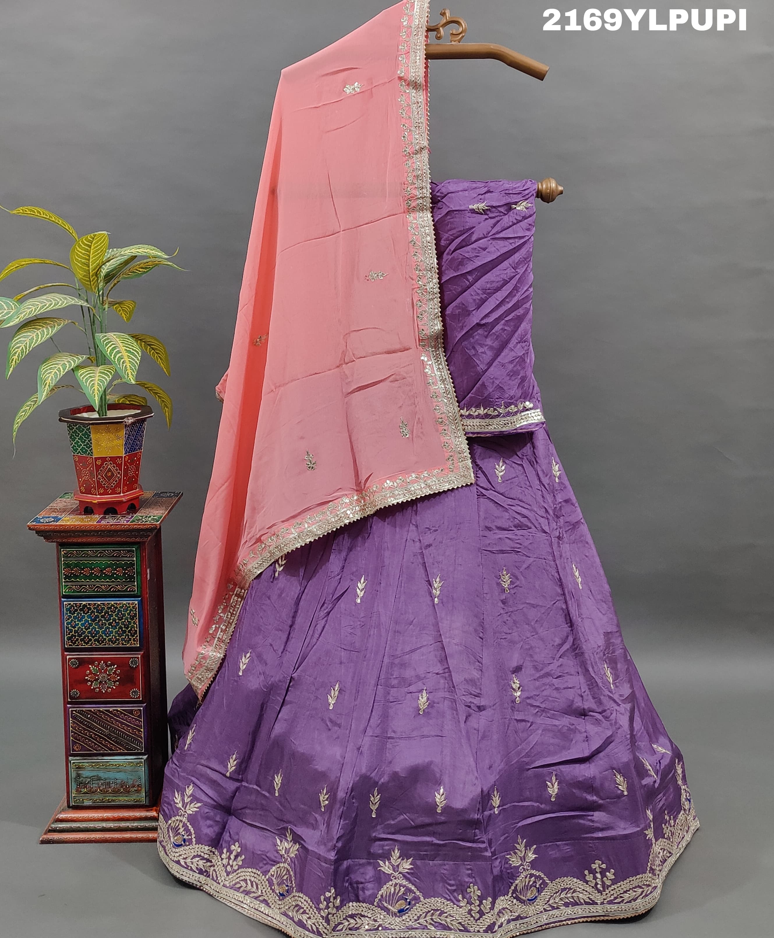 A traditional wear lehenga in purple with detailed embroidery and a pink dupatta.