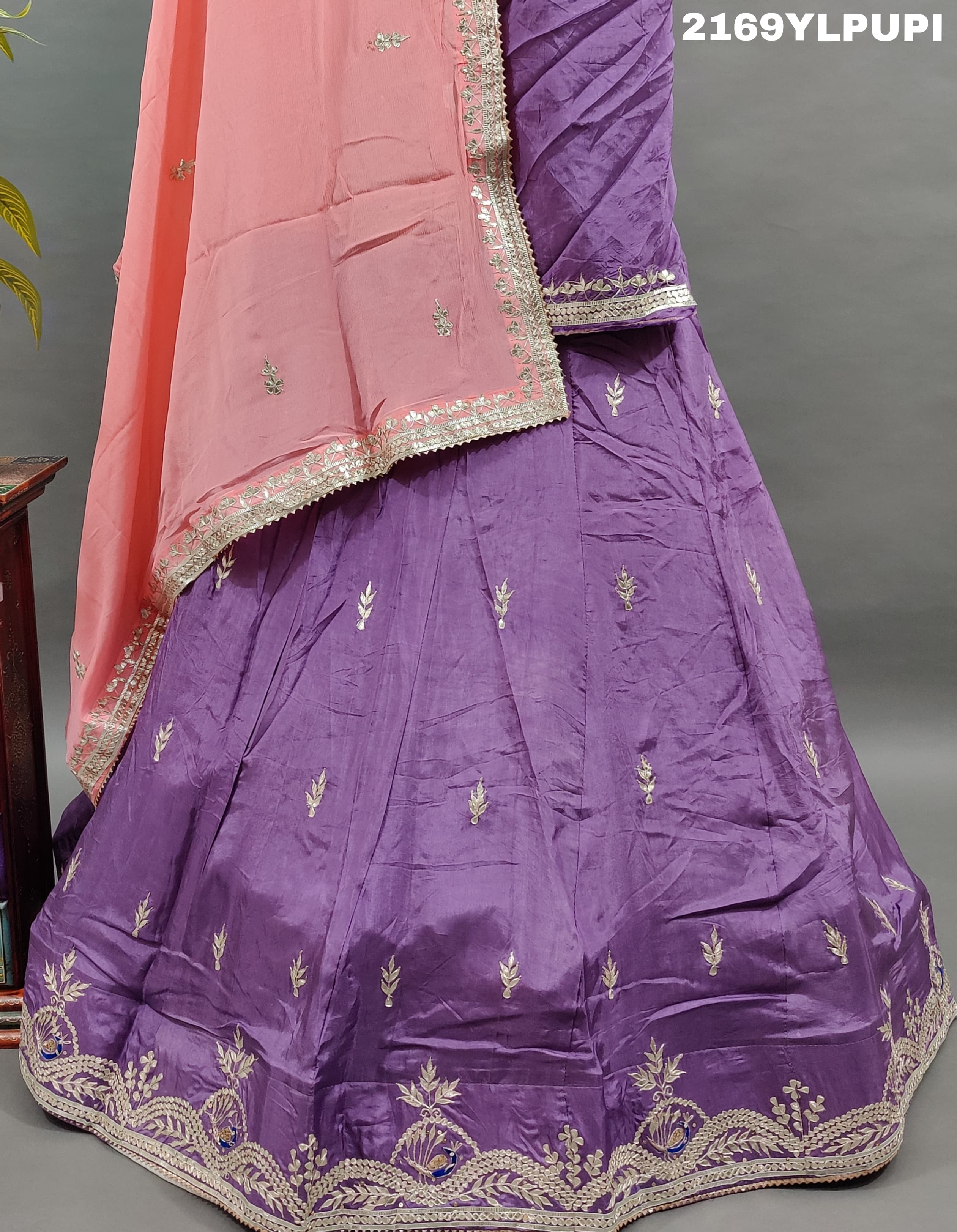 A traditional wear lehenga in purple with detailed embroidery and a pink dupatta.