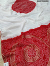 A traditional saree with red and white colors and intricate patterns, predominantly red at one end with a floral design.