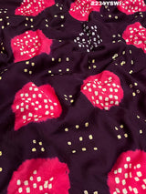 A purple and pink bandhani style saree with detailed patterns and a golden border.