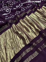 A purple and pink bandhani style saree with detailed patterns and a golden border.