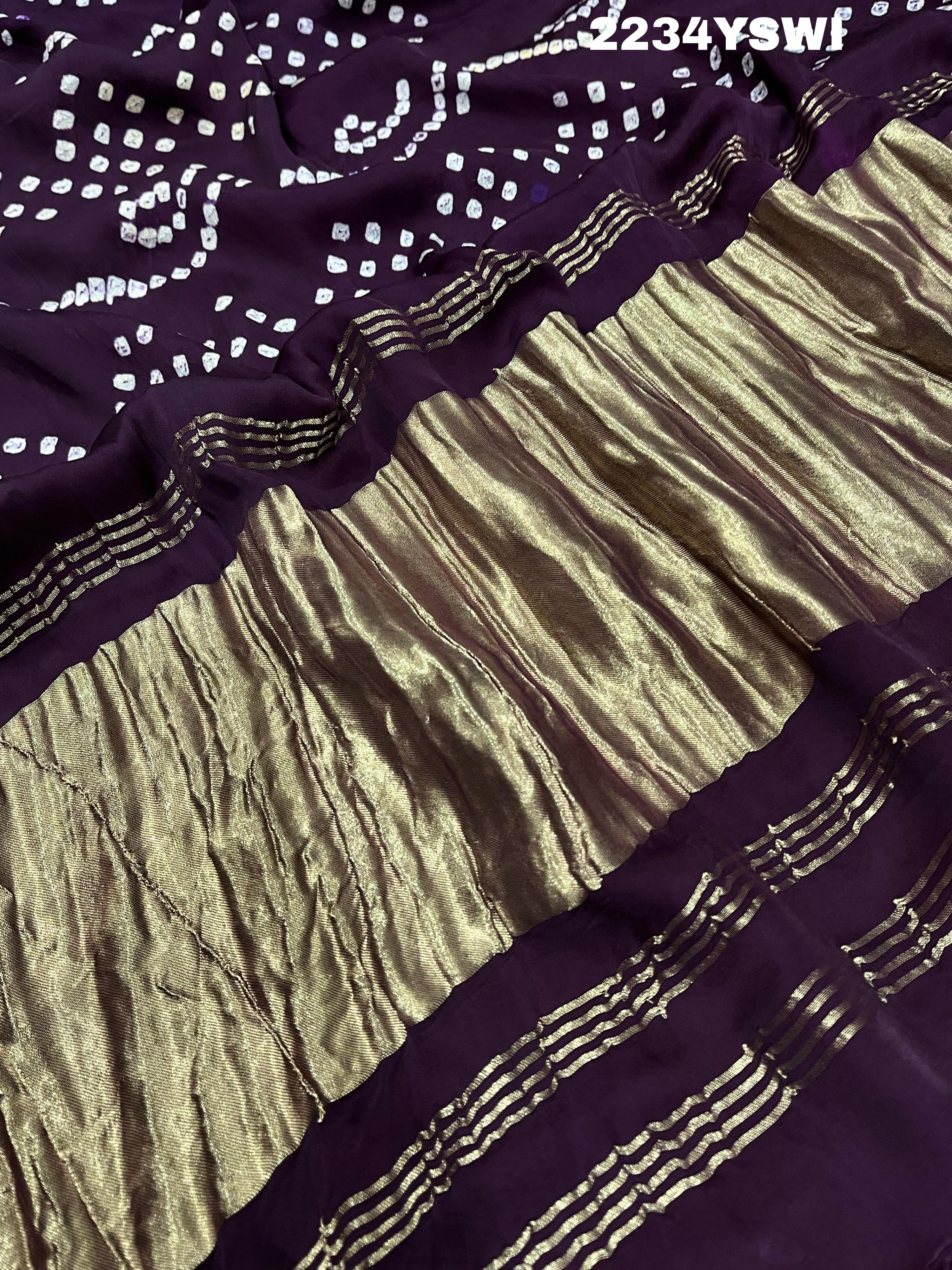 A purple and pink bandhani style saree with detailed patterns and a golden border.