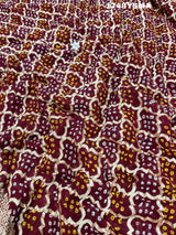 A maroon and gold saree with intricate geometric bandhej patterns and gotapatti handwork.