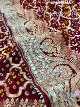A maroon and gold saree with intricate geometric bandhej patterns and gotapatti handwork.