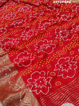 A red and silver bandhani style Dola silk saree with cutdana work and floral patterns, along with a golden border.