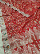 A red Banarasi style saree with gotapatti work, showcasing the detailed embroidery and pattern.