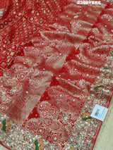 A red Banarasi style saree with gotapatti work, showcasing the detailed embroidery and pattern.