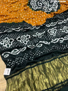 A bandhani style saree with black and yellow patterns on a fabric surface.