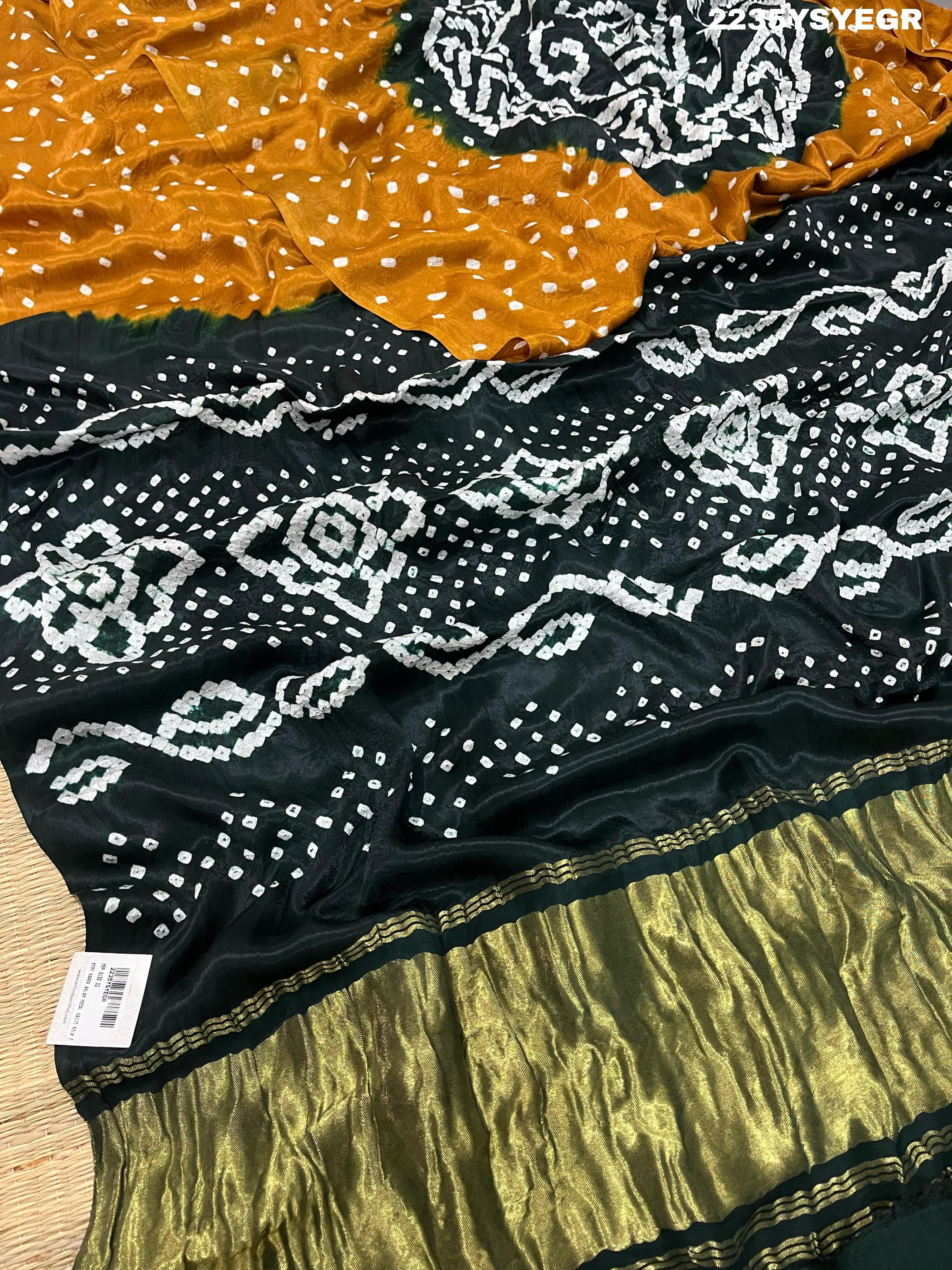 A bandhani style saree with black and yellow patterns on a fabric surface.
