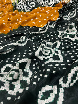 A bandhani style saree with black and yellow patterns on a fabric surface.