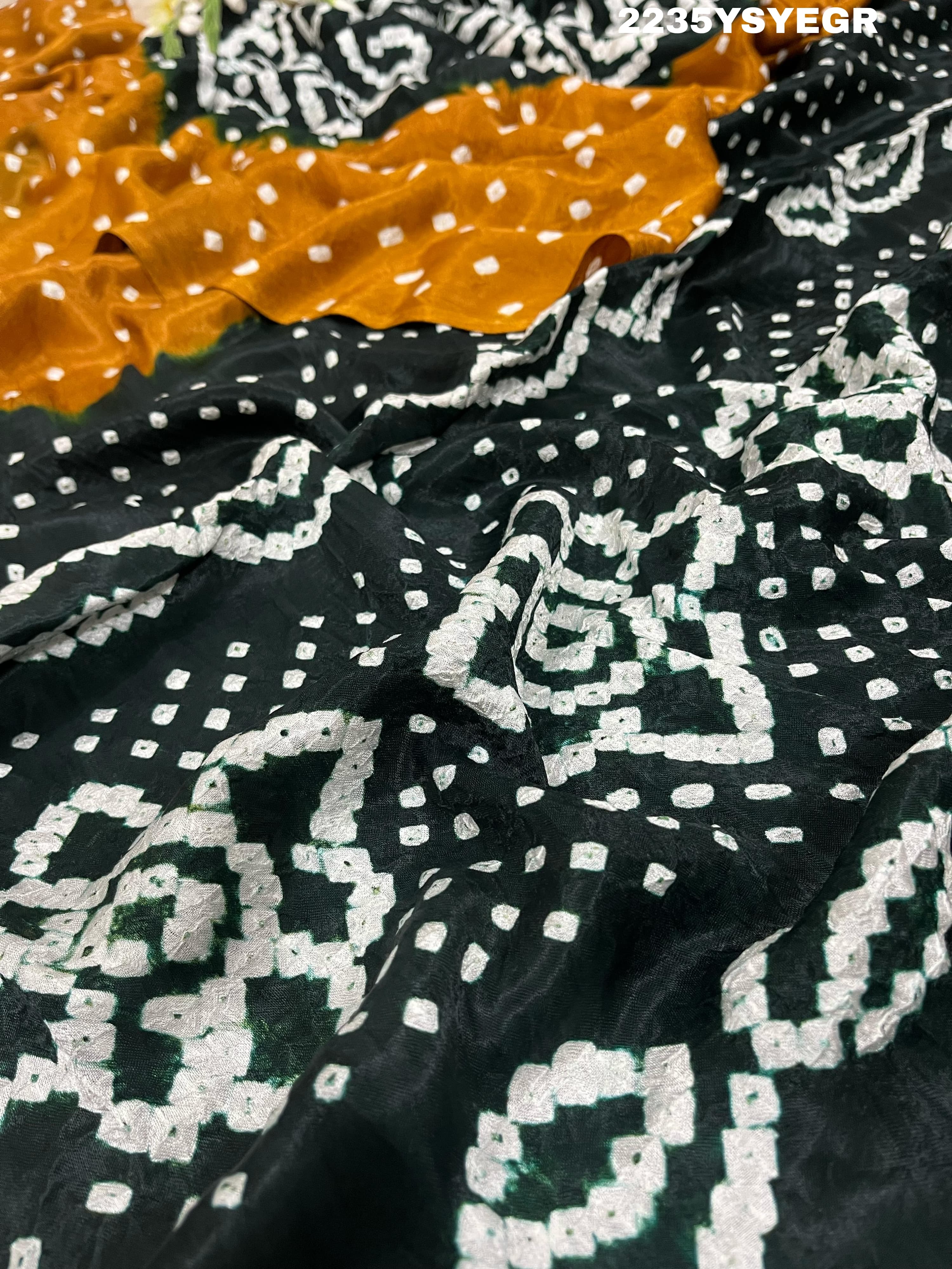 A bandhani style saree with black and yellow patterns on a fabric surface.